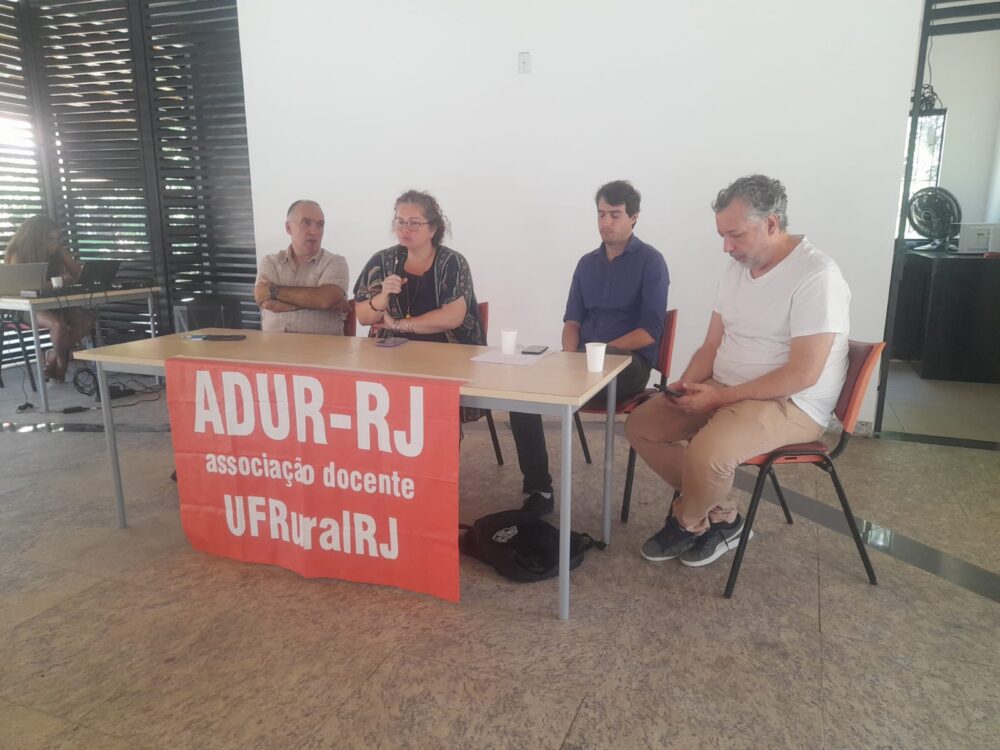 A mediadora do debate, Lilian Cordeiro; diretora da ADUR,  e os palestrantes Antonio José,Antônio José, Miguel Henriques e Alexandre Freitas (do Departamento de Ciências Econômicas da UFRRJ)